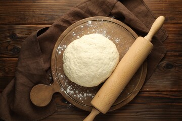 Fresh dough and rolling pin on wooden table, top view