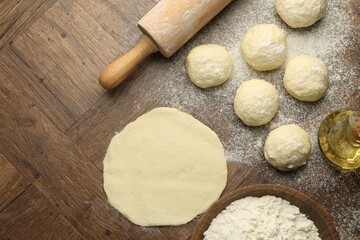 Fresh dough, rolling pin, flour and oil on wooden table, flat lay. Space for text