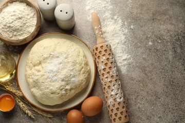 Fresh dough, ingredients and rolling pin on grey table, flat lay. Space for text