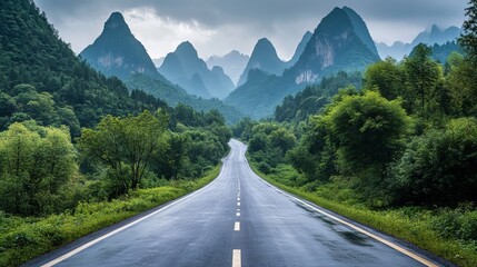Naklejka premium A road paved with asphalt cuts through a verdant forest, with towering mountains in the distance. This picturesque scene is found in Hangzhou, China.