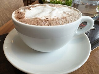 Frothy hot chocolate in white cup on wooden table at café
