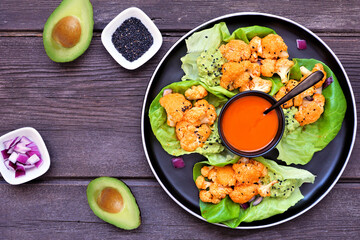Healthy lettuce wraps with buffalo flavor grilled cauliflower. Above view table scene over a dark wood background. Plant-based diet concept.