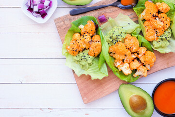 Healthy lettuce wraps with buffalo flavor grilled cauliflower. Overhead view table scene over a white wood background. Plant-based diet concept. Copy space.