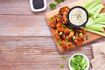 Healthy plant based honey garlic cauliflower wings with celery and ranch dip. Above view table scene with copy space over a rustic wood background.