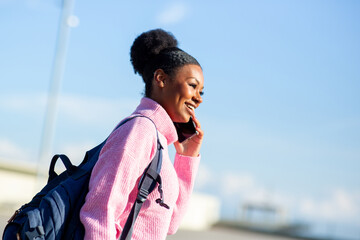 Young woman smiling and talking on smartphone while carrying backpack