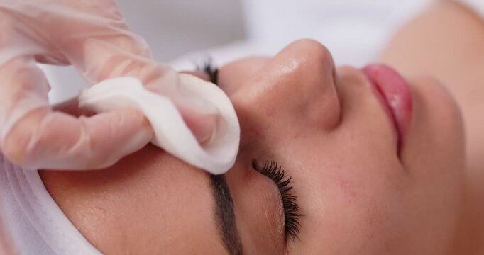 Dermatologist wipes a woman's forehead with a cotton pad, disinfects skin with antiseptic, takes a syringe, injects botulinum toxin to prevent mimic wrinkles. Beauty, face, aesthetic medicine concept