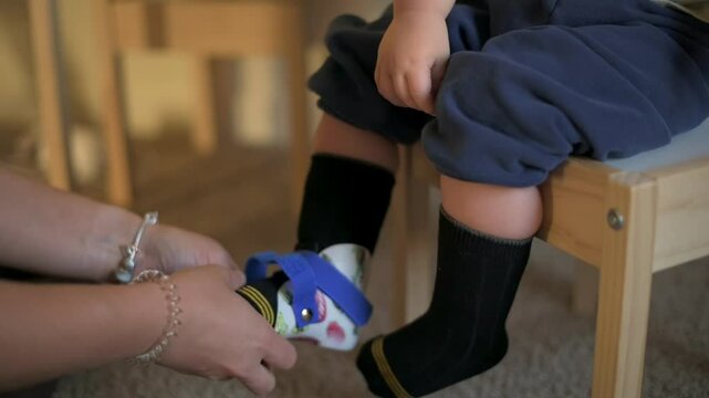 Adjusting Orthopedic Shoes for Child caregiver fastening orthopedic shoes on toddler seated on wooden chair supportive and caring moment highlighting child mobility and pediatric health.