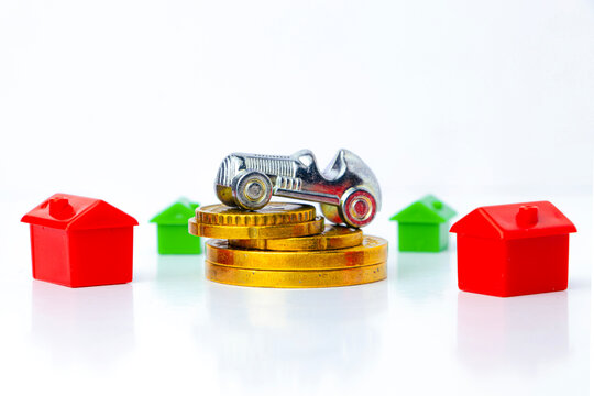 Miniature houses and car sit atop gold coins, representing real estate investment, property value, and financial growth. The image symbolizes market trends, homeownership