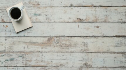 Overhead view of coffee cup and notebook on rustic white wooden table.