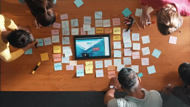 Top down view of programmer brainstorming and planning about web design while looking at tablet wireframe prototype. Aerial view of skilled developer team talking about digital application. Symposium.