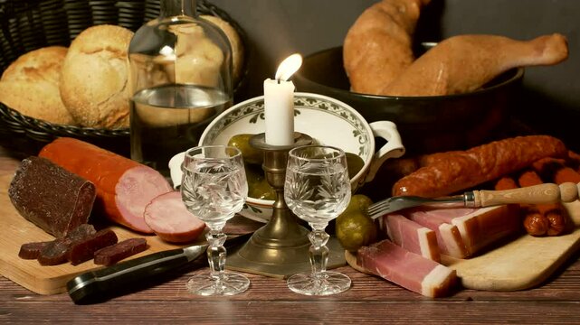 A stylized antique still life with meat, sausages, salami, lard and a glass of vodka.