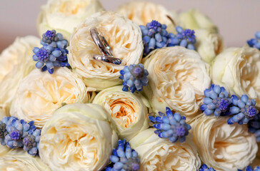 Golden wedding rings placed on cream roses with blue floral accents