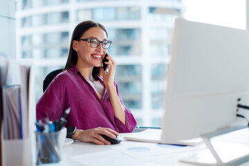 Businesswoman professional employee sitting at desk and making business call on cellphone and...
