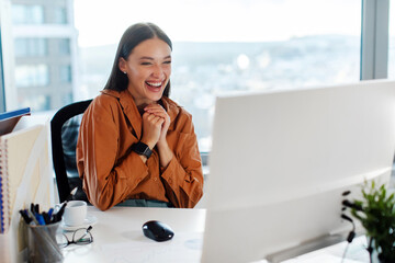 Emotional excited European businesswoman celebrating success, shaking clenched fists looking at computer monitor, reading great news