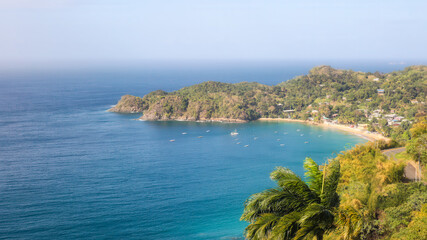 Fototapeta premium Panoramic view of Castara Bay with crystal clear water, sandy beaches, fishing boats, and green hills. Authentic escape for eco-tourists and travelers. Tobago island, Caribbean sea. Copy space.