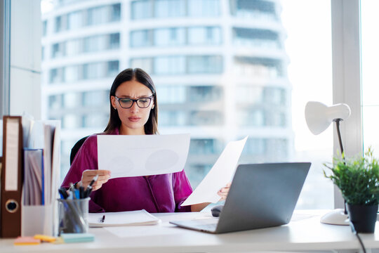 Focused woman manager, lawyer or company employee reading accounting bookkeeping documents and checking financial data, working in office