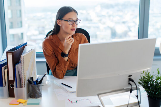Women in business. Concentrated European lady manager sitting in front of computer monitor, working in modern office interior