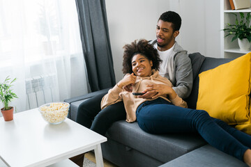 Happy African American couple enjoys quality time together while watching television. Man and woman...