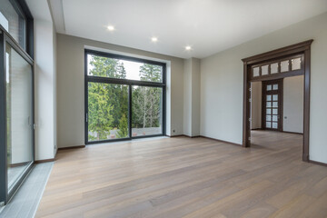Magnificent design of a room in a luxurious mansion. Wide doorway, panoramic windows with a view of green trees. Unfurnished.
