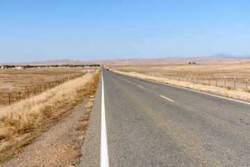 Straight highway running between dry grassy fields in California central valley on a sunny autumn day