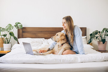 Woman working remotely from home with golden retriever dog on bed
