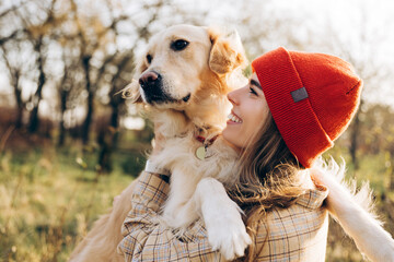 Woman wearing red beanie holding golden retriever in autumn park