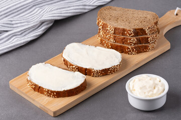 Creamy spread on slices of dark bread displayed on a wooden board with a bowl of dip beside it