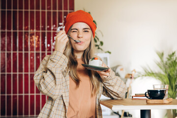 Cheerful young woman tasting delicious cake in modern cafe