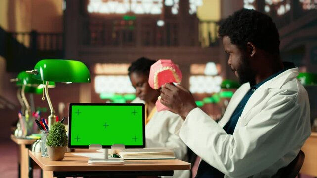 Medical student learns dentistry practices on a dummy jaw model next to mockup, developing dental qualifications through techniques. Study tools for exam preparations. Camera B.