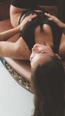 Portrait of young beautiful model posing in black lingerie and stockings on sofa in white room....