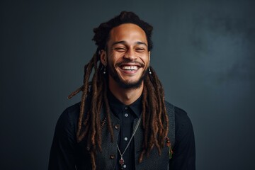 Obraz premium Portrait of a young male musician with dreadlocks smiling and showing his white teeth on a dark background