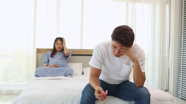 Husband sits with head lowered, stressed, holding condom, looking depressed because he can't have sex with his pregnant wife : Concept preventing impact during pregnancy.
