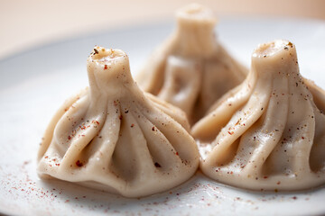Traditional khinkali dumplings on a plate with pepper seasoning sprinkled on top and soft focus background