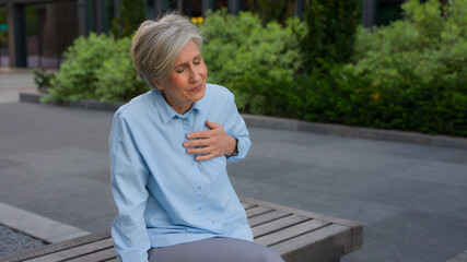 Caucasian senior old mature woman sick unhealthy businesswoman in city bad feeling pain in chest heart attack ill business lady suffer heartburn heartache retired female with health problem outdoors