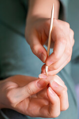 girl hand gently cares for her nails using a wooden orange stick with a pointed tip, showcasing a delicate and detailed manicure process