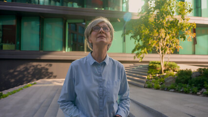 Fototapeta premium Portrait business lady Caucasian 50s adult mid age gray-haired mature woman senior old female looking around in city center successful inspired elder businesswoman smiling look away dreaming outdoors