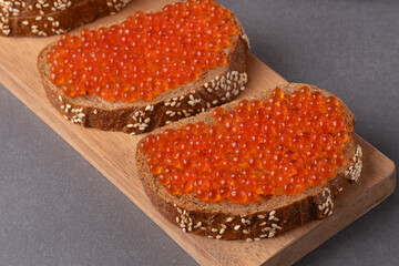 Delicious rye bread topped with bright red caviar served on a wooden board for a gourmet snack experience