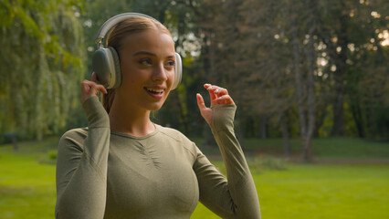 Happy sport girl runner jogger listen music in headphones in city park nature Caucasian woman turn on audio for sports training run running outdoors fitness exercise healthy lifestyle morning habit
