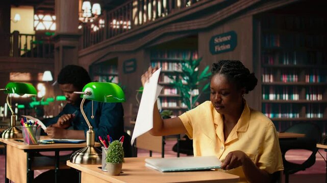 African american pupil highlighting key words from the class notes, creating a summary to study easily and memorize the lesson theory. Student using a learning technique in the library. Camera A.