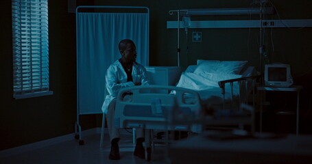 Young African doctor sits in a dark hospital room.
