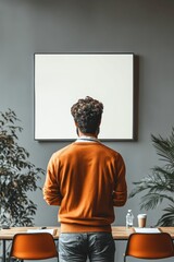 Man facing blank board, orange sweater, modern office.
