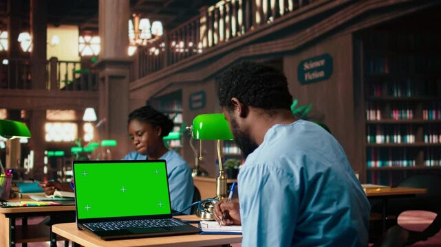 Black medical student reviews case files in the library next to copy space screen, preparing for a lecture or study session on medical practices. Med school pupil learns for a career. Camera A.