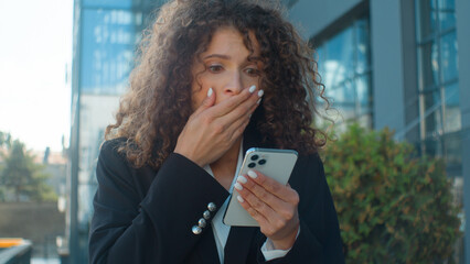 Caucasian businesswoman with phone in city business networking outdoors excited amazed wonder good...