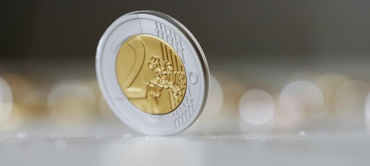 Two euro coin spinning around on a table. Wealth, investment and money. Close up of a single coin that stops spinning in focus. Slow motion video in 4k - Powered by Adobe