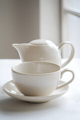 Fototapeta premium A white teacup and teapot set on a white table, bathed in soft, natural light.