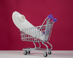 Clitoral vibrator in miniature shopping cart on pink background. 