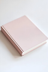 Fototapeta premium A closed rose gold notebook rests on a white surface. Perfect for minimalist branding or stationery designs.