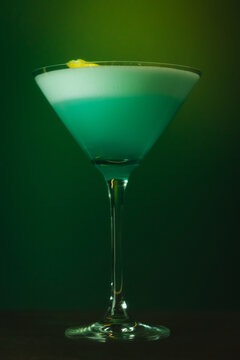 Elegant Blue Cocktail in Martini Glass against a vibrant green gradient background