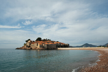 Sveti Stefan island with pebble beach and medieval Mediterranean fishing village at sunrise