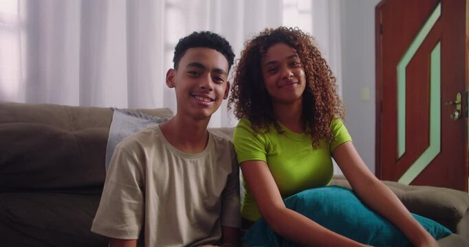 Teenager brother and sister smiling warmly while sitting on couch, representing sibling companionship and cheerful family interaction
